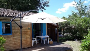 Una casetta in legno con un patio, un tavolo e due sedie sotto un grande ombrellone.