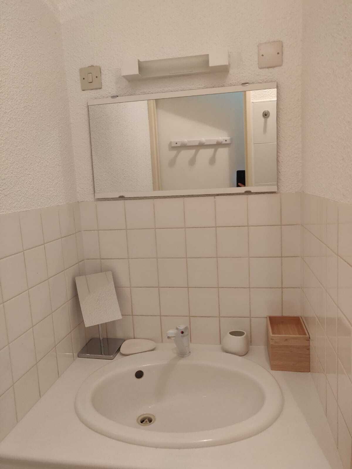 Une petite salle de bain avec un lavabo blanc, un miroir, un porte-serviettes et une petite boîte en bois.