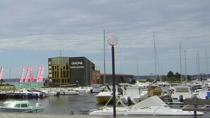 Una marina con barche ormeggiate, un edificio con la scritta 'GUCA Centre Nautique' e cielo sereno.