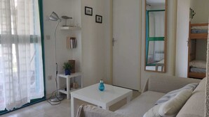 Una stanza piccola e luminosa con un divano, un tavolino, una TV a parete, una libreria e uno specchio.