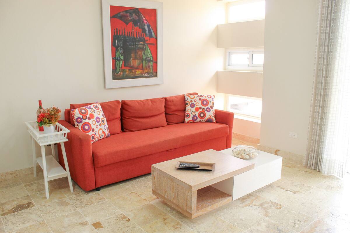 A living room with a red sofa, a white coffee table, and a framed artwork on the wall.