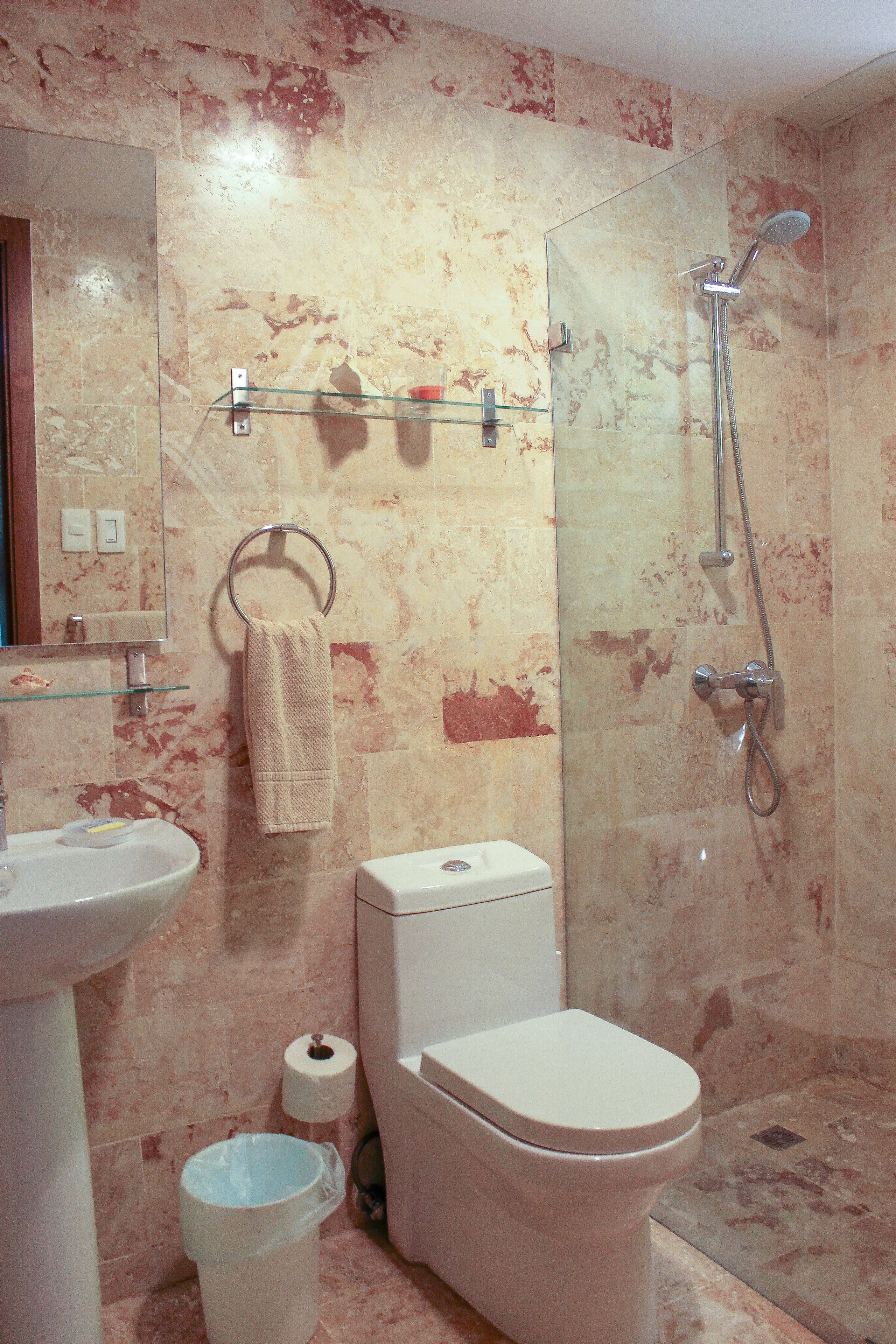 A bathroom with a marble wall, a glass shower enclosure, a toilet, a sink, and a towel rack.