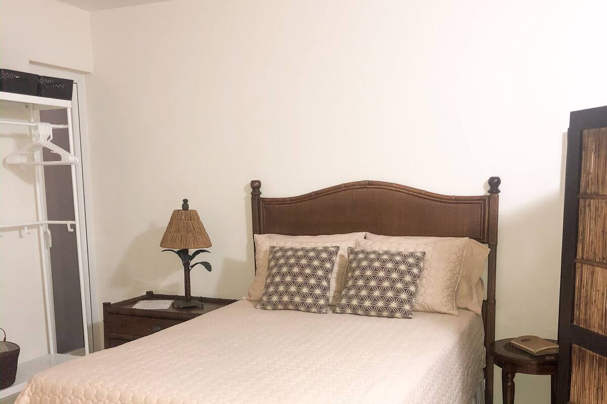 A bedroom with a large bed, a bedside table, a lamp, a wardrobe, and a bench.