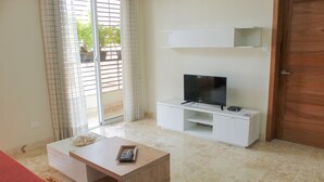 A living room with a TV on a white stand, a wooden coffee table with a remote, and a red sofa. - Villago Residences (Santo Domingo)