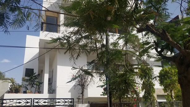 Un edificio moderno con fachada blanca, entrada vigilada y un árbol en primer plano.