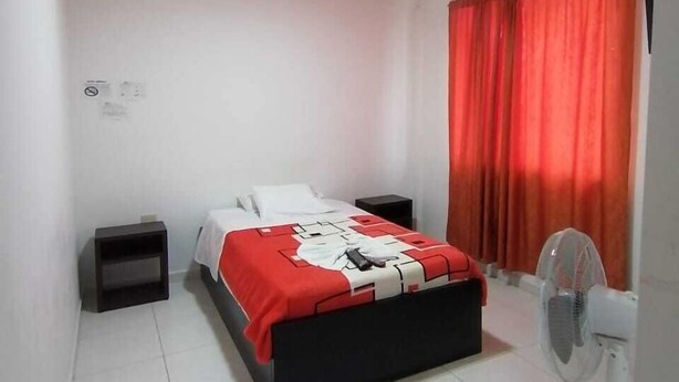 A bedroom with a bed, a nightstand, a fan, and a red curtain. - Hotel Central - Mocoa (Mocoa)