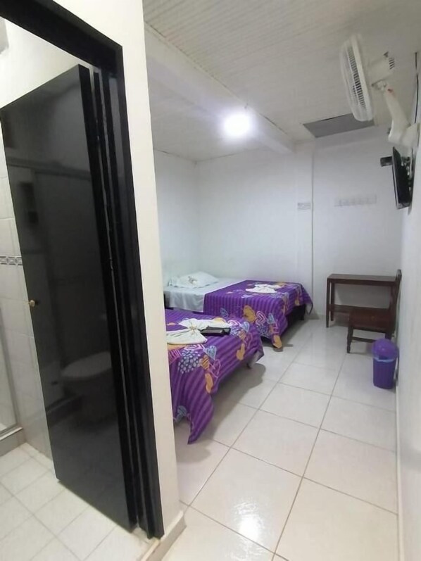 A room with two beds, a small table, a wall-mounted fan, and a trash bin. - Hotel Central - Mocoa (Mocoa)