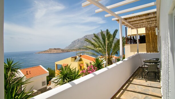 Ein Balkon mit Blick auf das Meer und ein Berg, ausgestattet mit einer Pergola, Gartenmöbeln und tropischen Pflanzen.