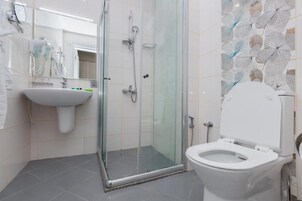 Een moderne badkamer met een douchecabine van glas, een witte wastafel en een toilet.