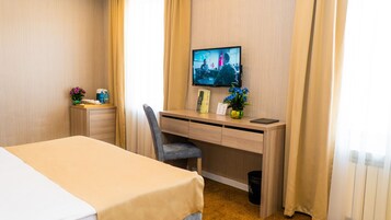Hotelkamer met een bed, bureau met computer, stoel, televisie en een klein tafeltje met bloevasen.