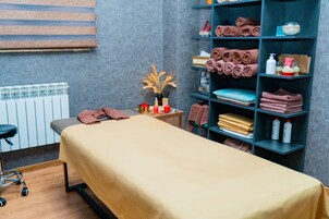 Een massageruimte met een massagetafel, planken met handdoeken en flesjes lotion.