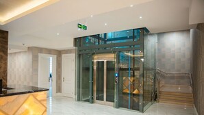 A modern lobby with a glass elevator, marble flooring, and a staircase. - Grand Midway Hotel (Baku)