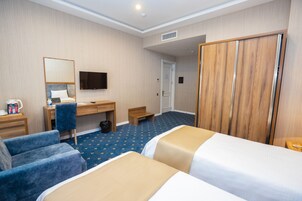 Una habitación de hotel con dos camas, un escritorio, una silla, un televisor y un armario.