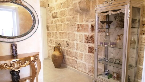 A room with a stone wall, a wooden console table with a vase, a mirror, and a glass cabinet with decorative items. - Borgo Salentino (San Vito dei Normanni)