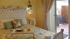 A bedroom with a tufted headboard, a bedside table, a tray with a glass and a bowl, and a view of an outdoor patio with furniture. - Borgo Salentino (San Vito dei Normanni)