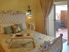 Un dormitorio con cabecera capitonada, una mesita de noche, una bandeja con un vaso y vistas a un patio exterior.