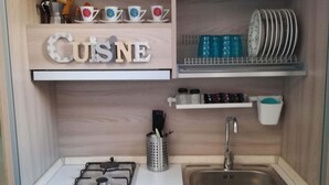A compact kitchen with a gas stove, a sink, and wooden cabinetry. There are shelves with decorative items and kitchenware. - Borgo Salentino (San Vito dei Normanni)