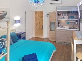 A bedroom with a bed, a desk, and a kitchenette.