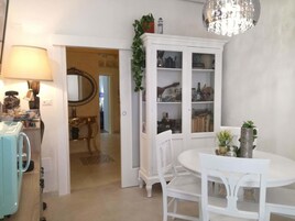 Un comedor con una mesa y sillas blancas, una araña y un aparador con puertas de cristal.