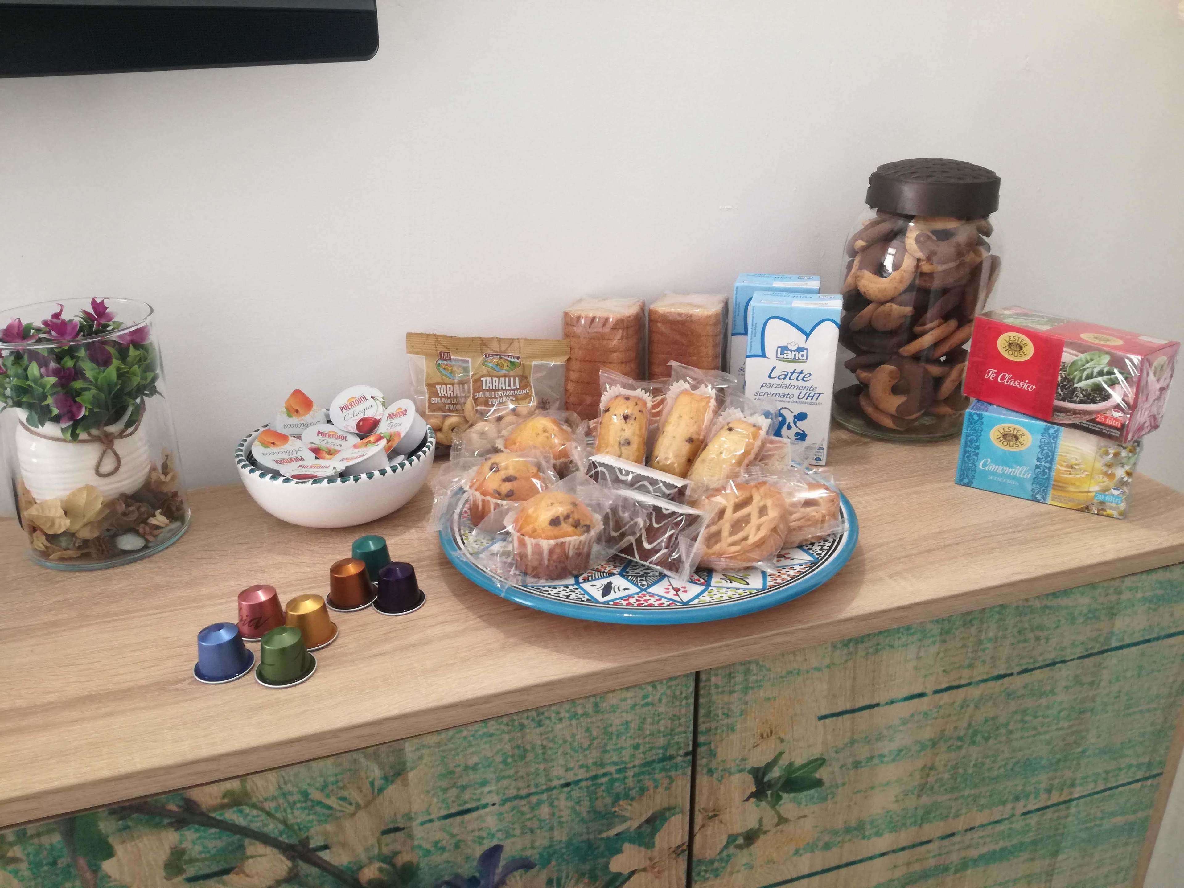 A wooden table with various food items, including packaged snacks, bread, and a decorative plant in a glass jar.