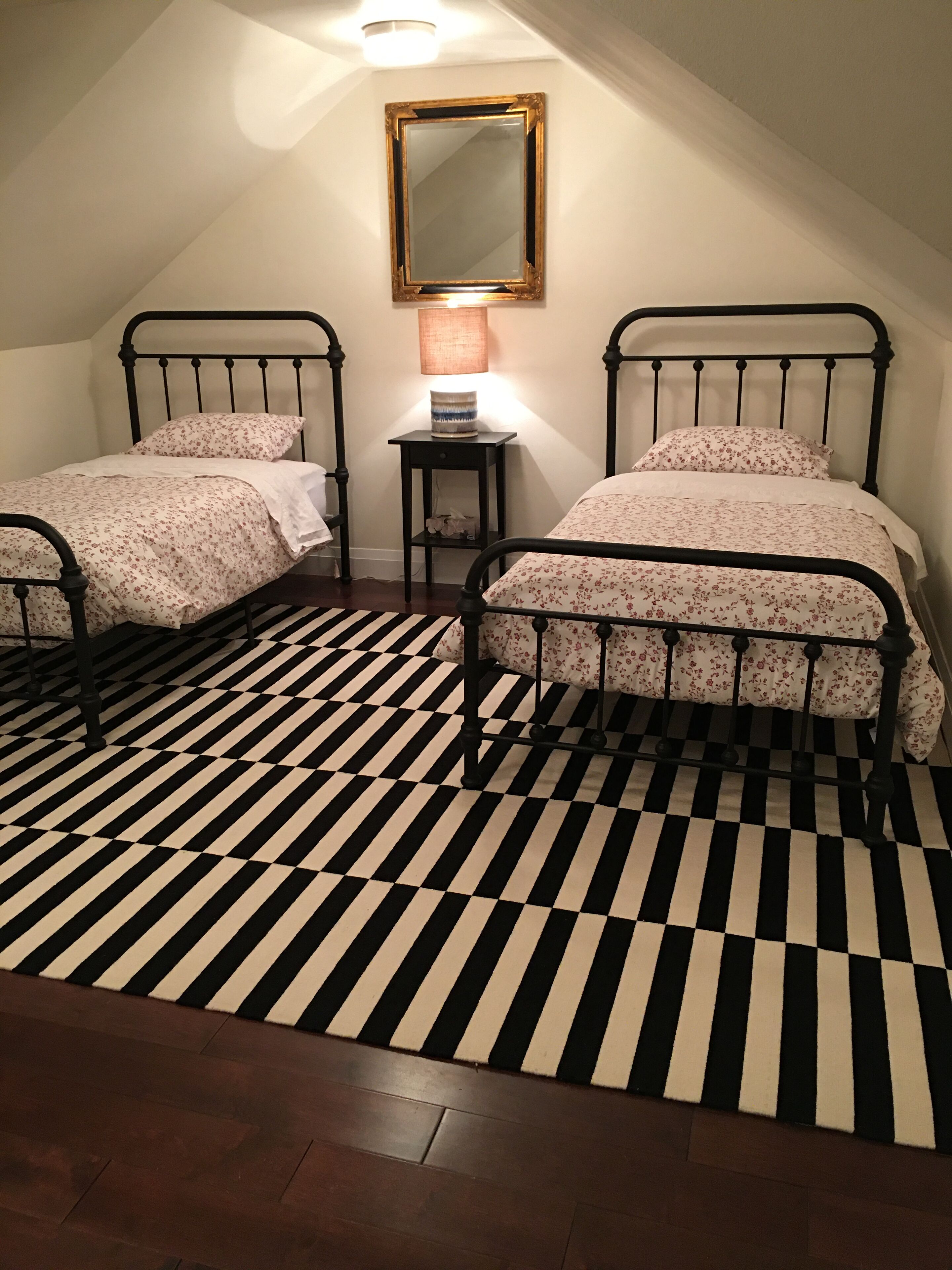 Een slaapkamer met twee bedden, een zwart-wit geruite vloer, een klein tafeltje met een lamp en een spiegel aan de muur.