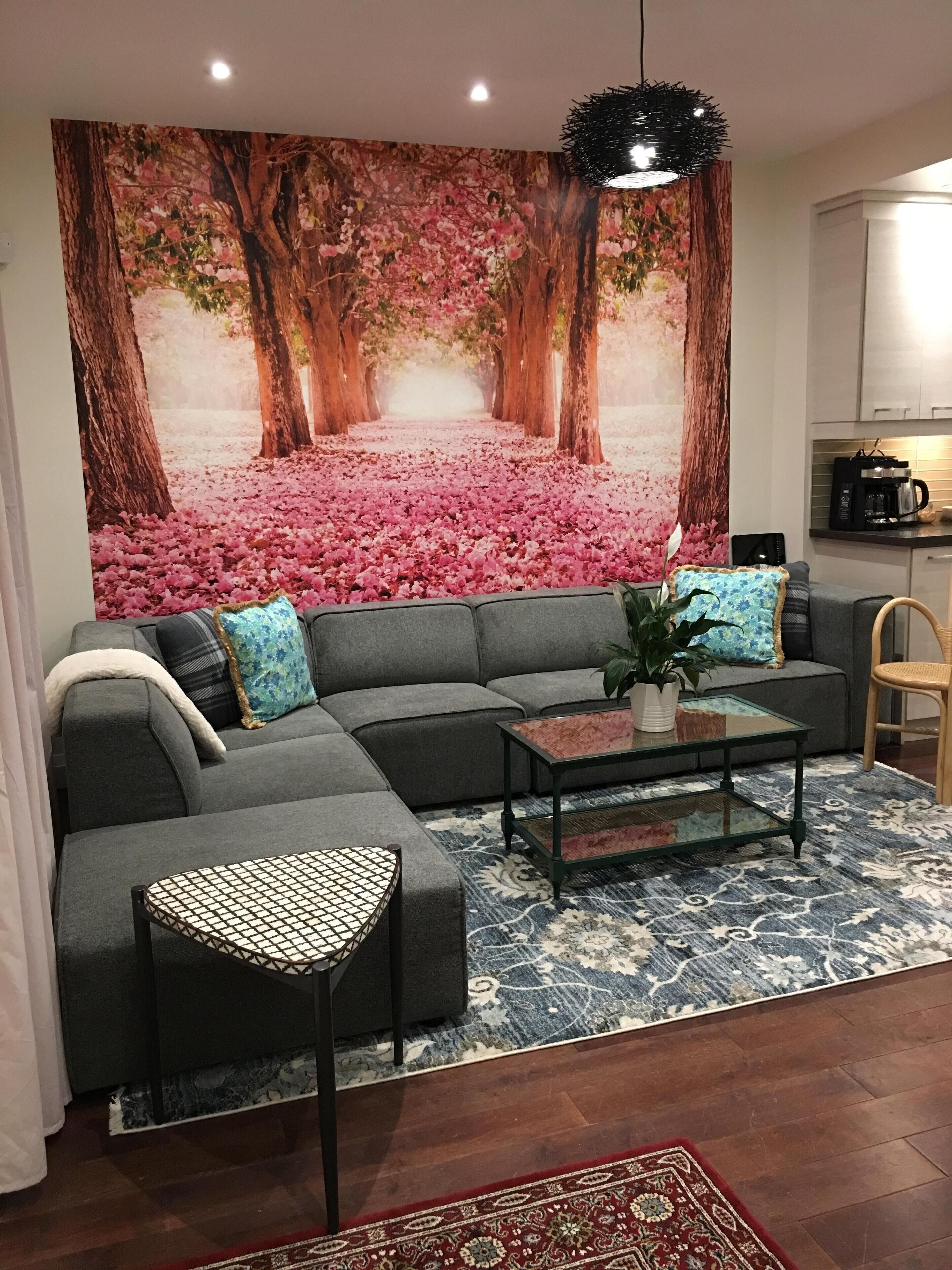 A living room with a sectional sofa, a coffee table, and a large floral tapestry on the wall.