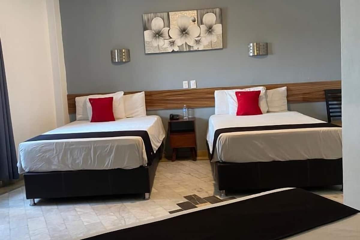 A hotel room with two beds, a ceiling fan, a wall-mounted artwork, and a small bedside table.