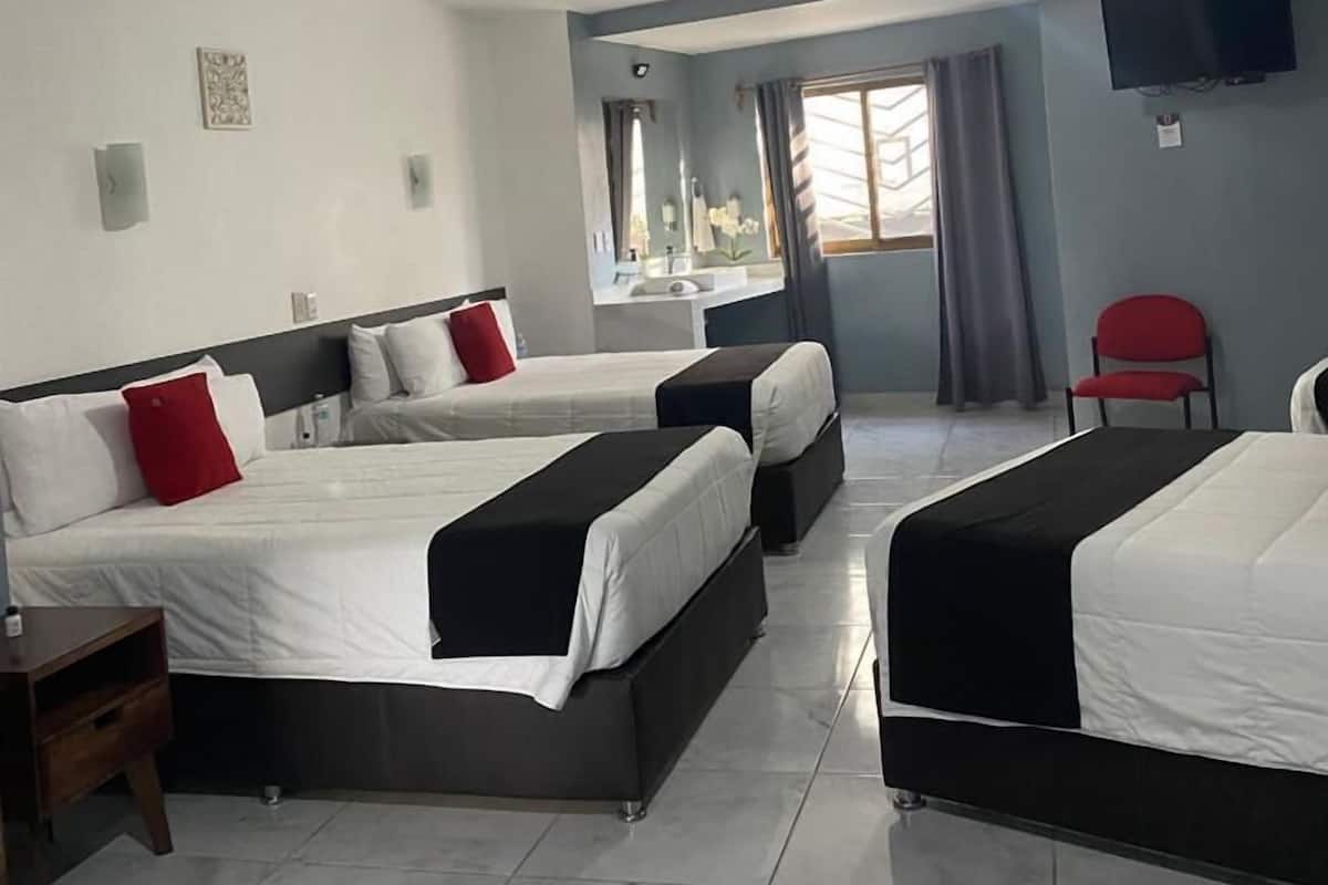 A hotel room with three beds, a ceiling fan, a TV, and a window with curtains.