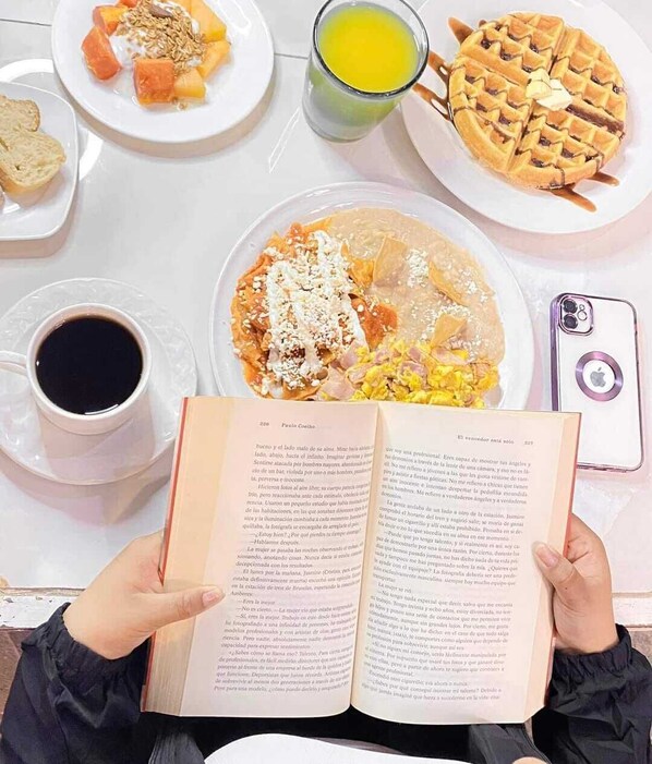 A person reading a book at a table with breakfast items including waffles, toast, and a cup of coffee.