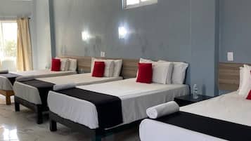 Habitación de hotel con cuatro camas dispuestas en fila, piso de baldosas de mármol y un equipo de aire acondicionado en la pared.