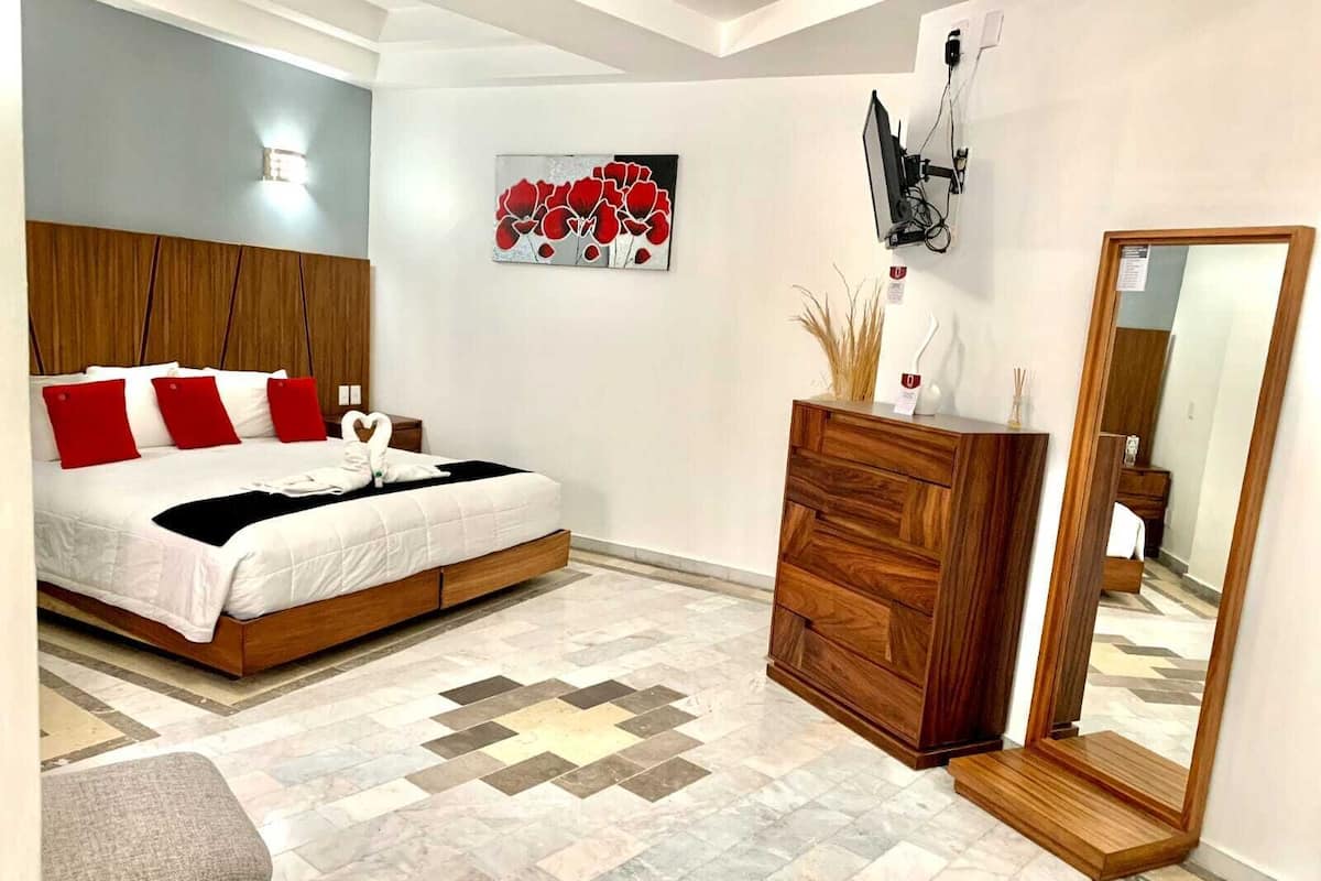 A modern bedroom with a bed, wooden headboard, a dresser, a mirror, and a wall-mounted TV.