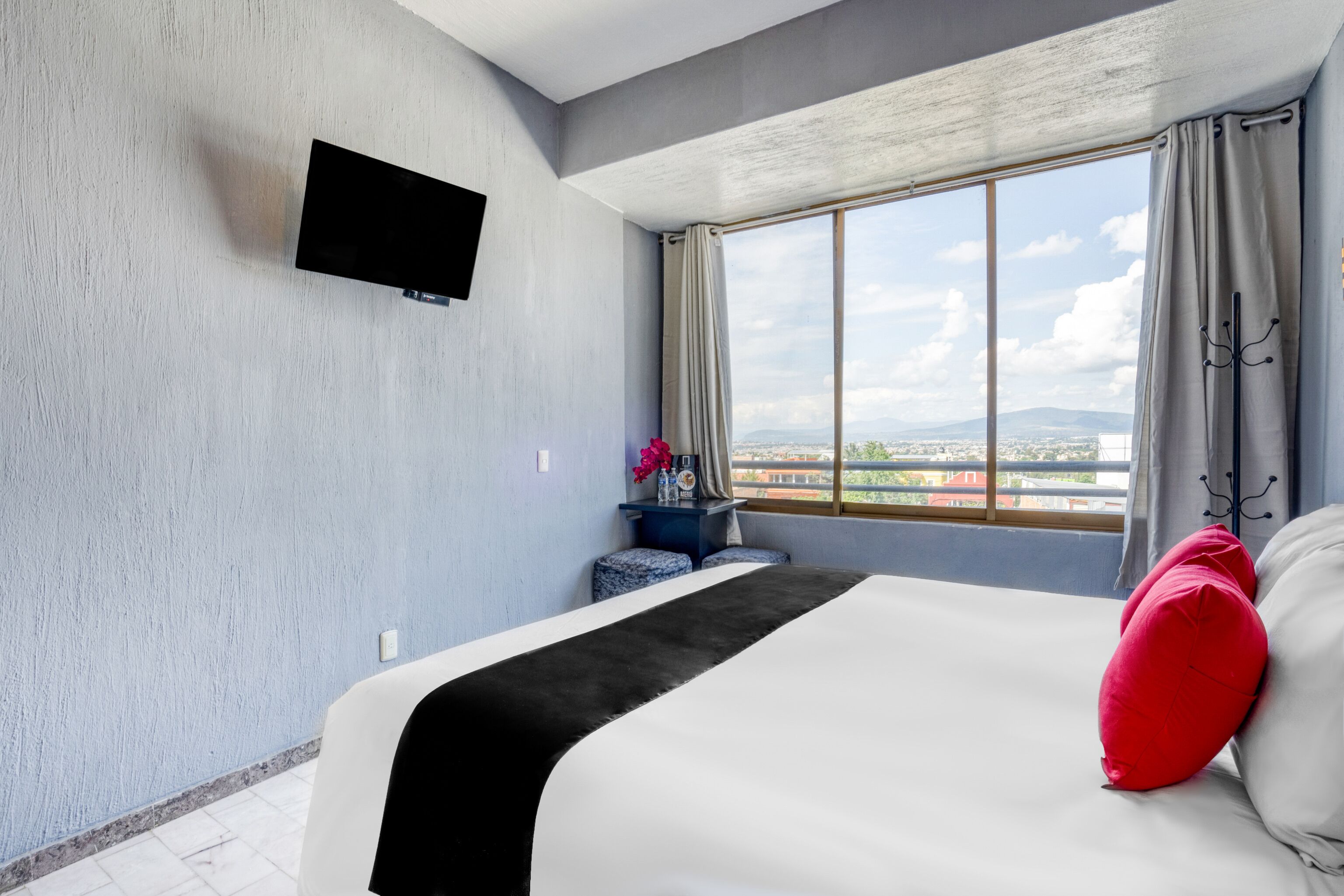 Habitación de hotel con una cama grande, un televisor de pantalla plana en la pared y una ventana con vistas a la ciudad.