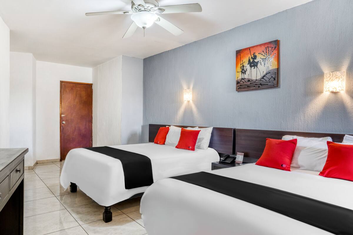 A hotel room with two beds, a ceiling fan, a painting on the wall, and a nightstand with a phone.