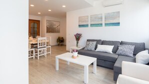 A modern living room with a grey sofa, white coffee table, and a dining area with white chairs. - Apartment on the beachfront overlooking the sea of Alboran, in the Malagueta. (Málaga)