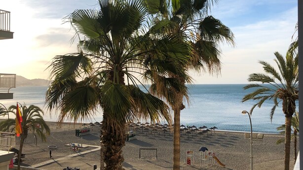 A view of a beach with palm trees, a parking area, and a building with balconies. - Apartment on the beachfront overlooking the sea of Alboran, in the Malagueta. (Málaga)