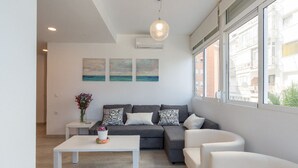 A modern living room with a grey sofa, white armchairs, a white coffee table, and a large window with a view of buildings. - Apartment on the beachfront overlooking the sea of Alboran, in the Malagueta. (Málaga)