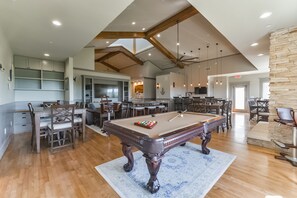 A spacious indoor area with a pool table, dining tables, and chairs. There are ceiling fans, recessed lighting, and a stone accent wall. - Harborwalk Lodge (Hitchcock)