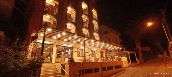 A multi-story building with a balcony and outdoor seating area, illuminated by string lights.