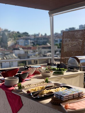 A balcony with a buffet setup, including plates, bowls, and a grill.
