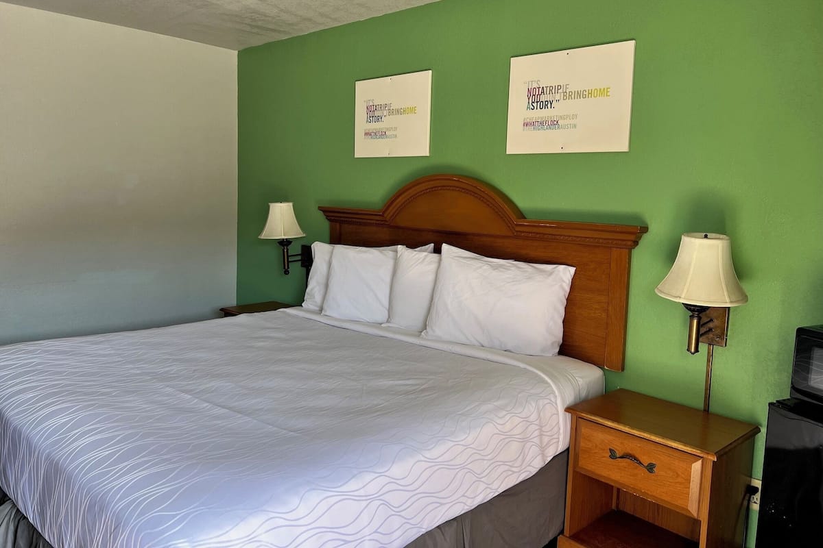 Ein Hotelzimmer mit einem großen Bett, zwei Wandlampen, einem Nachttisch aus Holz und zwei Bildern an der Wand.