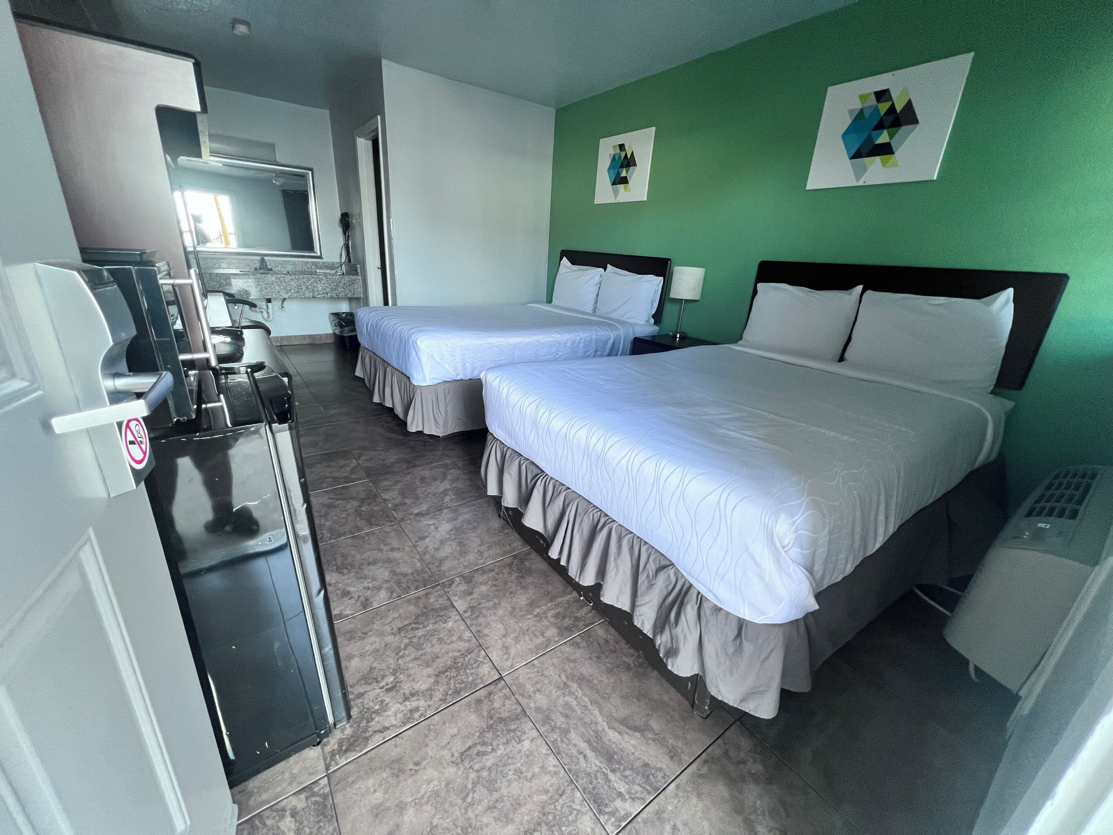 A hotel room with two beds, a desk with a computer, and a green wall with artwork.