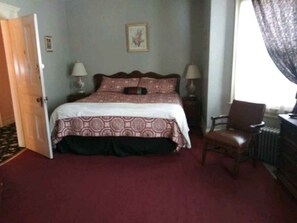 A bedroom with a bed, two bedside tables, a chair, a radiator, and a door.