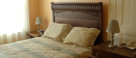 Una cama bien tendida con ropa de cama floral, una lámpara de noche y una mesita de noche con un teléfono.