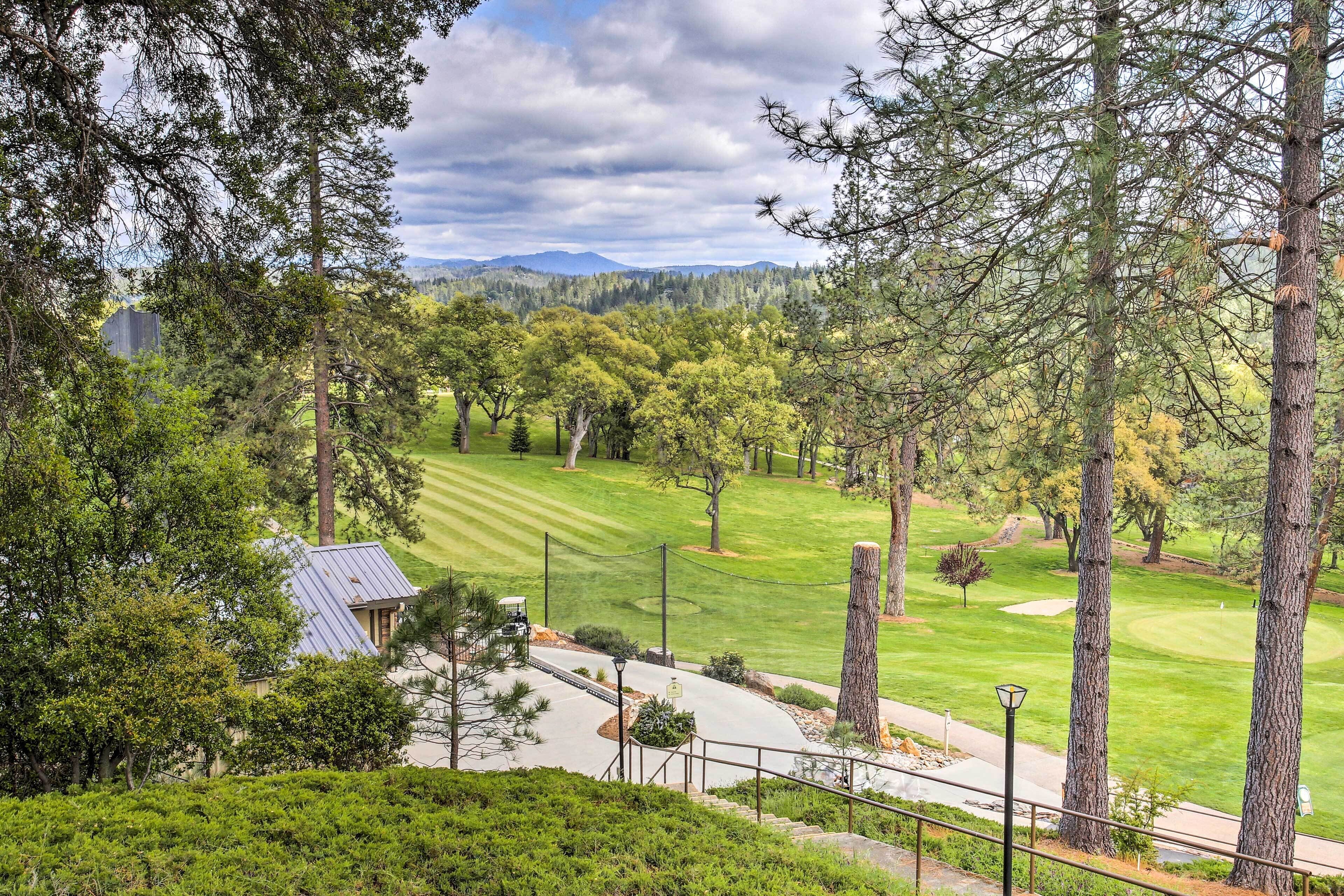 Un campo de golf con un club de campo, rodeado de altos árboles y montañas al fondo.