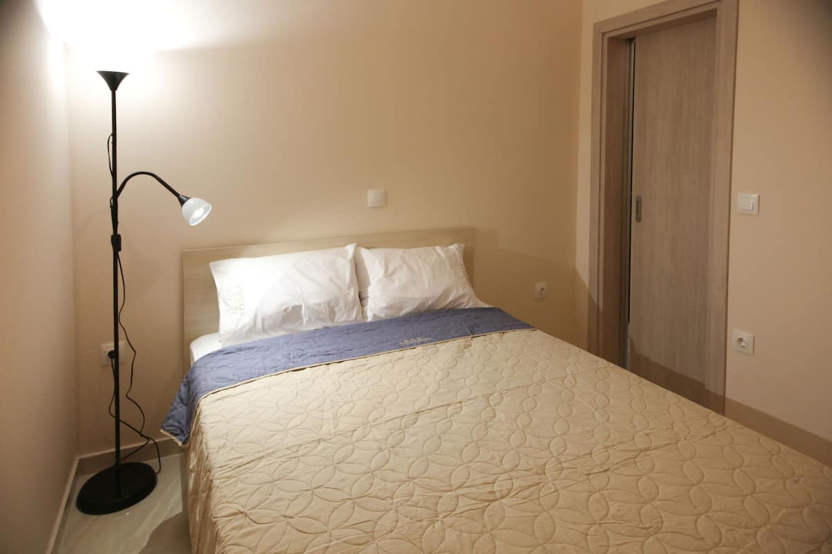A bedroom with a bed, a floor lamp, and a door.