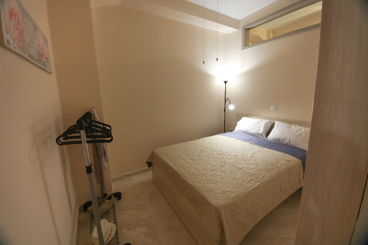 A bedroom with a bed, a nightstand, a lamp, and a wall-mounted rack.