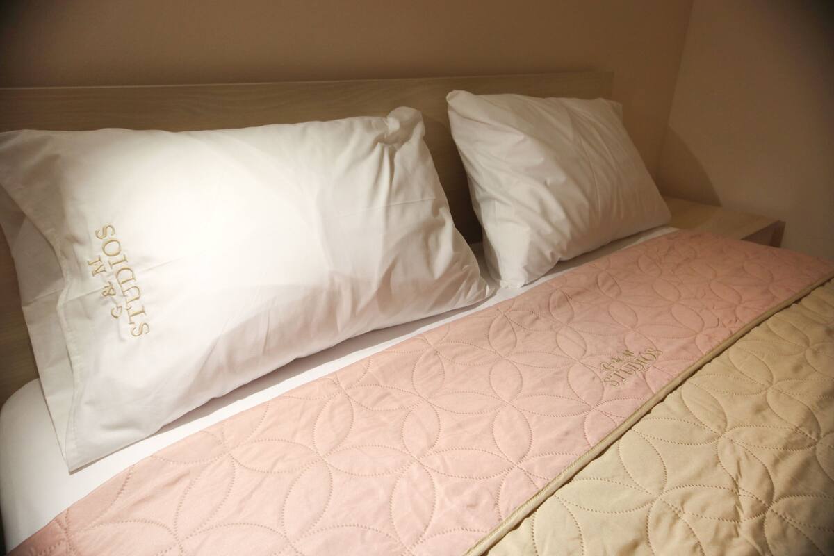 A bed with two white pillows and a pink and beige quilted bedspread.