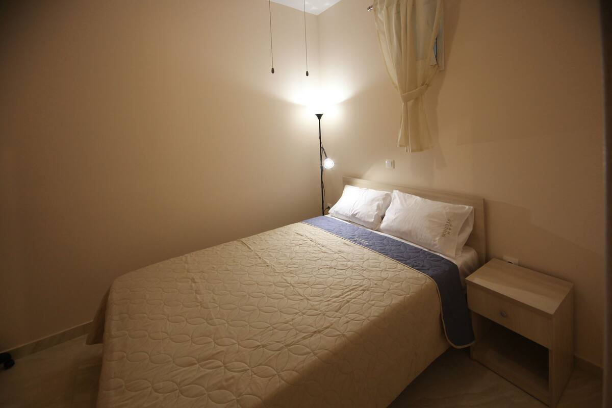 A neatly made bed with a patterned quilt, a bedside table with a lamp, and a hanging curtain.