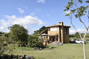 A rustic house with a patio, surrounded by a garden and a car parked nearby. - Mawasi Finca (Villa de Leyva)