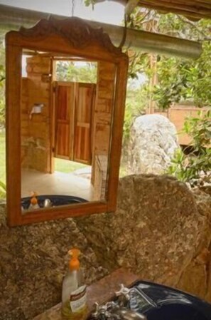 A bathroom with a wooden-framed mirror, a bottle of lotion, and a towel on a stone counter. - Mawasi Finca (Villa de Leyva)